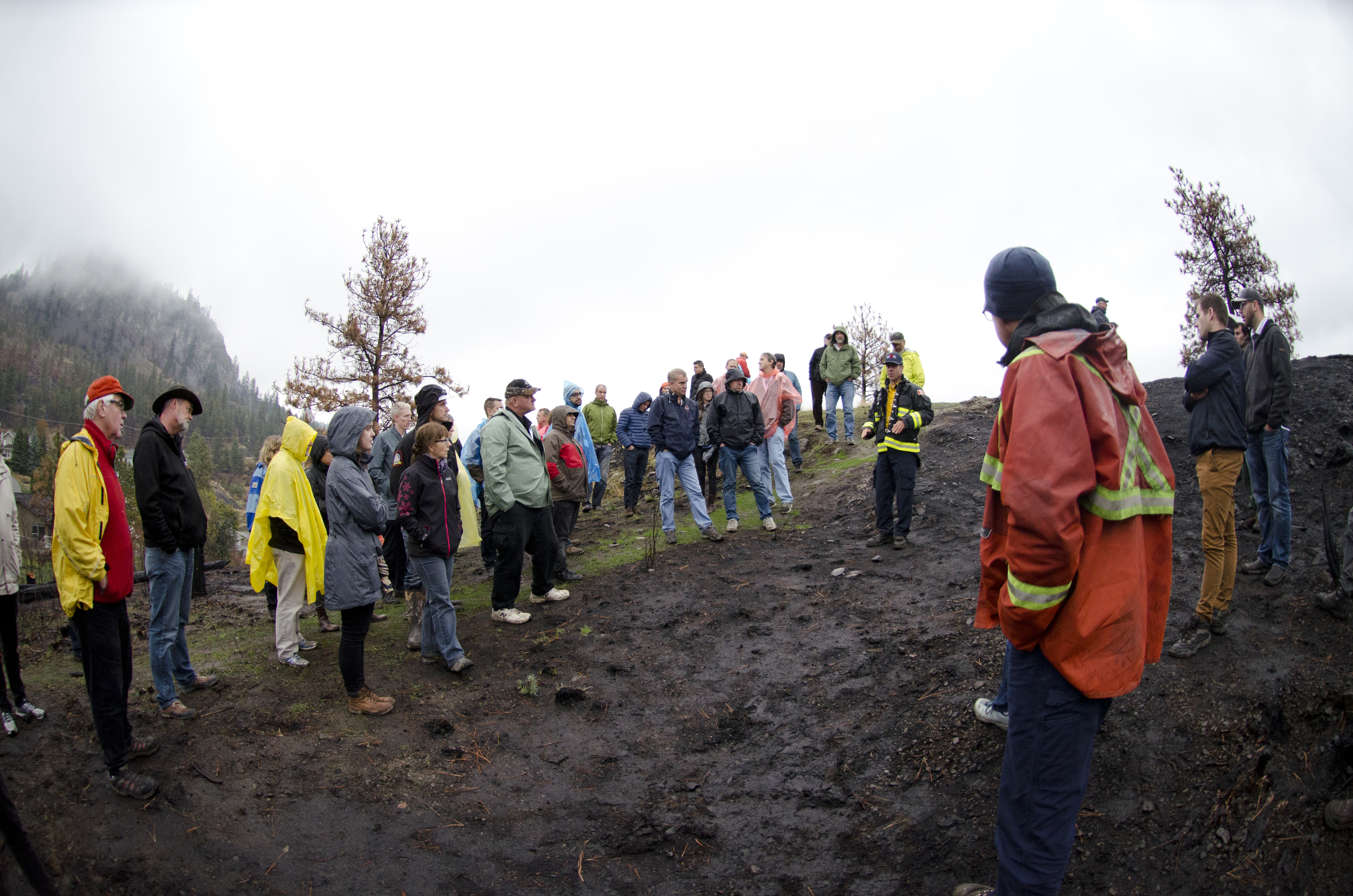 Field trip attendees at a wildfire conference stand around in the rain at a burn site.
